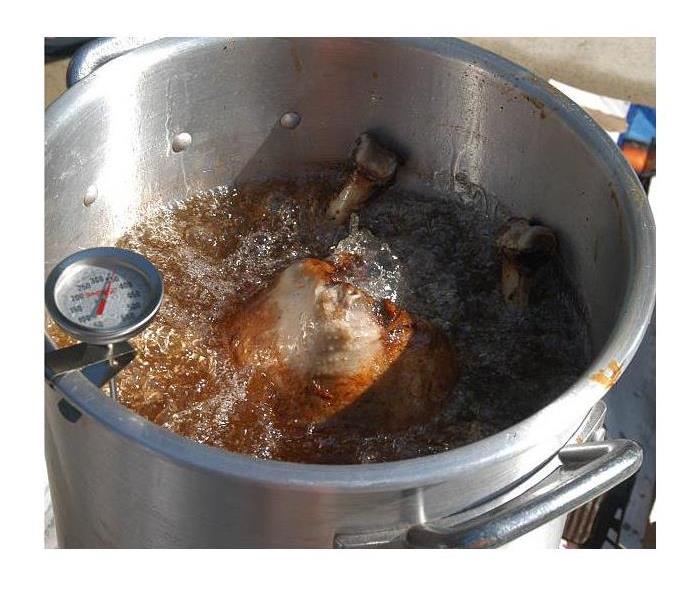 A person with black gloves pulls a turkey out of a fryer